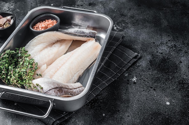 Raw haddock fish fillets whitefish meat in kitchen tray with thyme Black background Top view Copy space