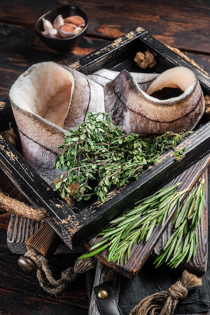 Raw Haddock fish fillets in wooden tray with rosemary and thyme. Wooden background. Top view.