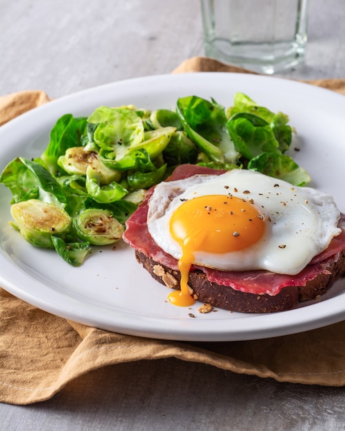 Photo raw ham and egg toast with brussel sprouts on a white plat