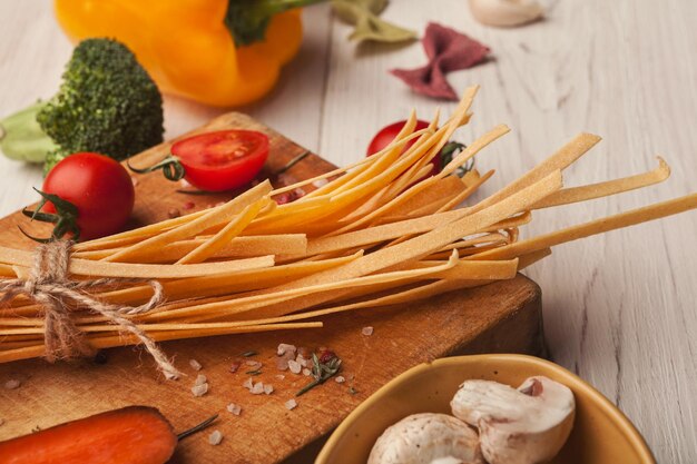 Raw handmade orange tagliatelle with carrot juice, tomatoes, broccoli, mushrooms and spices on white wooden table. Cooking pasta background, copy space