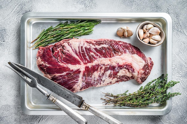 Raw hanger or onglet beef meat steak in steel tray with herbs. White background. Top View.