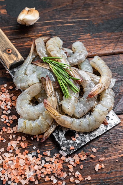 raw headless tiger shrimps prawns on a butcher cleaver. dark wooden background. top view.
