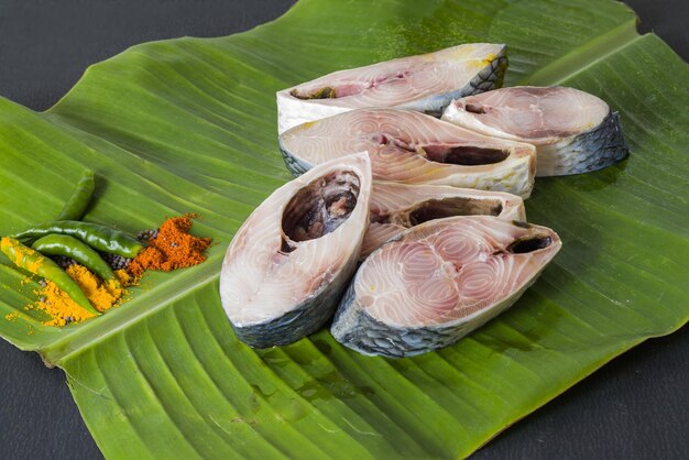 Raw hilsa fish cut into pieces kept on banana leaf for cooking shot taken in studio with copy space background and spices