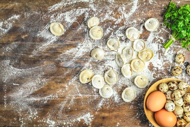 Raw homemade delicious traditional italian ravioli dumplings with meat and set ingredients on dark wooden old surface top view copy space