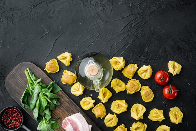 Raw homemade Tortellini with cured ham set, on black table, top view flat lay