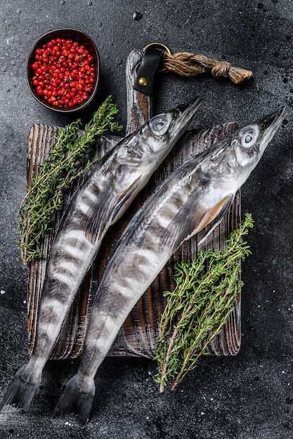 Raw icefish on a wooden cutting board. Black background. Top view.