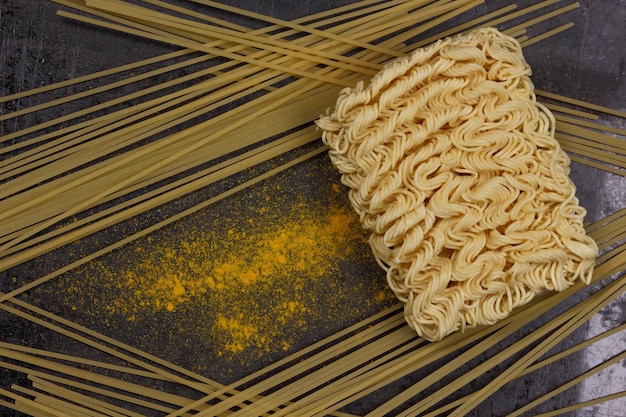 Raw instant noodles and spaghetti with yellow spices on a dark background Closeup View from above
