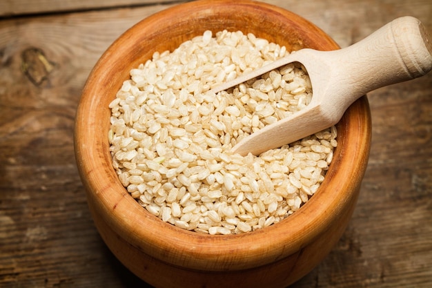 Raw integral rice in a wooden bowl with a wooden scoop on a wooden table