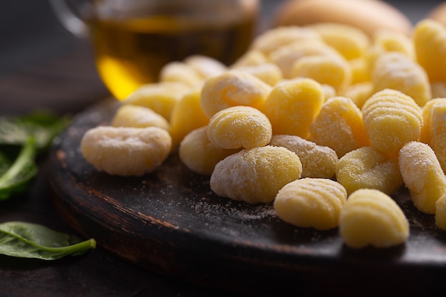 Raw italian gnocchi on a dark wooden background, close up, selective focus. They are dumplings, usually oval, made from wheat flour dough with egg