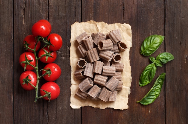 Raw italian  pasta, basil and cherry tomatoes on wooden table