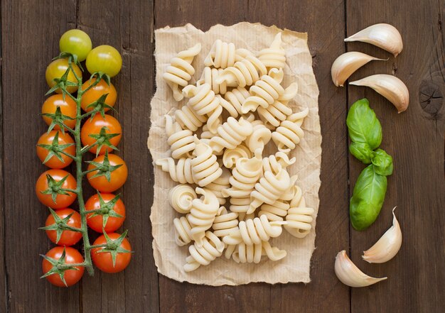 木の表面に生のイタリアンパスタ、バジル、野菜