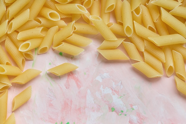 Raw Italian penne pasta on pink surface