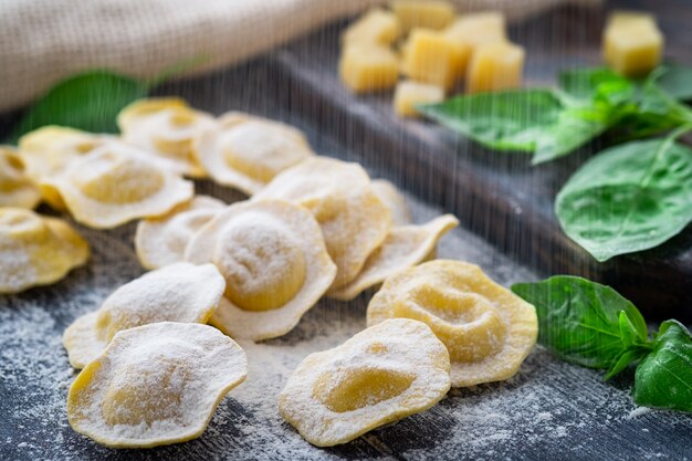 Raw Italian ravioli pasta with parmesan and basil on a wooden board with flour