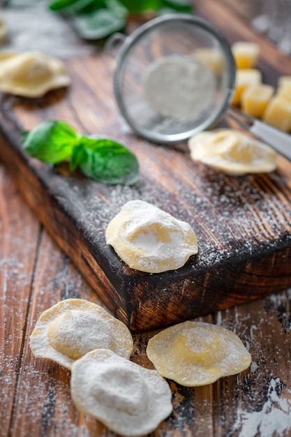 パルメザンチーズとバジルの小麦粉で木の板に生のイタリアのラビオリパスタ