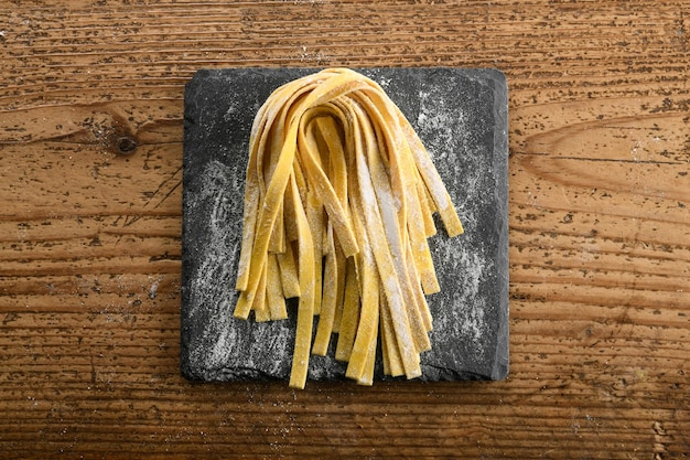 Raw Italian tagliatelle pasta placed on floury board on table