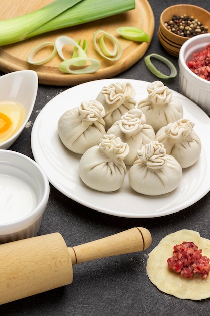 Raw khinkali dumplings on white plate and ingredients for making dumplings Leek on the board Top view Black background