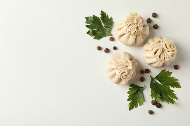 Raw khinkali, pepper and parsley on white table