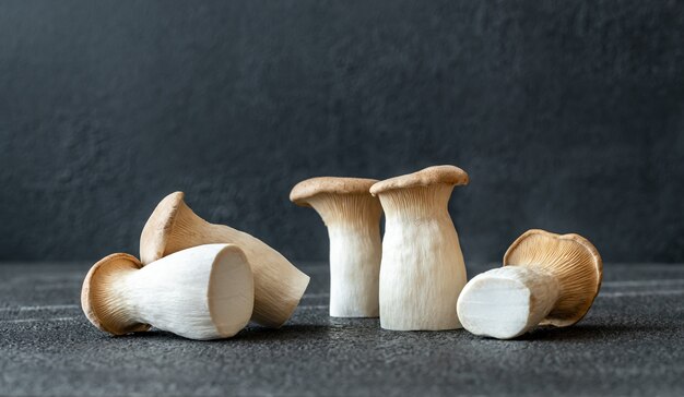 Raw king oyster mushrooms on dark surface