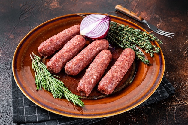 Raw kofta meat kebabs sausages on a plate with herbs. Dark background. Top view.