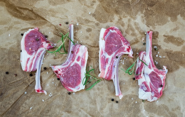 Raw lamb chops. Rack of Lamb with rosemary and spices over oily craft paper .