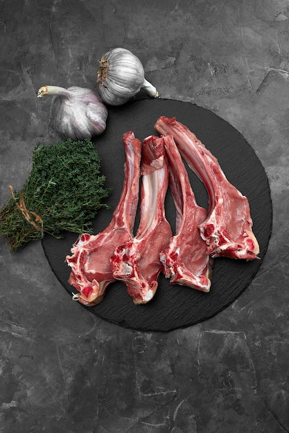 Photo raw lamb chops with garlic, herbs on black ceramic plate over white stone gray table. top view. with copy space.