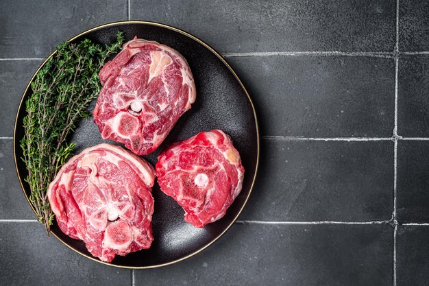 Photo raw lamb gerdan lamb neck chops on a plate with herbs black background top view copy space