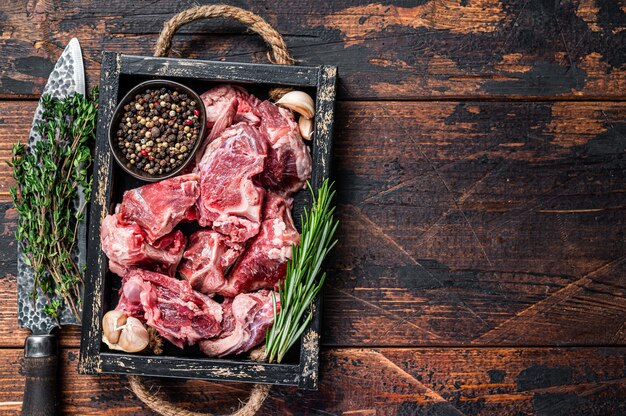 Raw lamb or goat meat diced for stew with bone. Dark wooden background. Top view. Copy space.