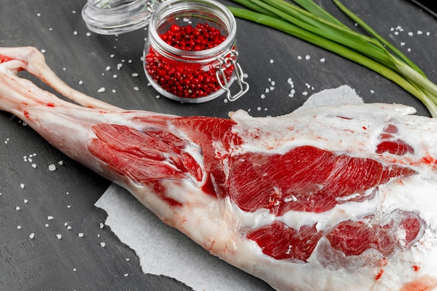 Raw lamb leg on black stone background