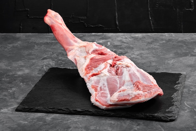 Raw lamb leg on marble cutting board Dark background Side view