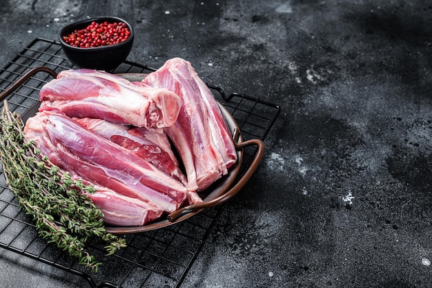 Stinco di coscia di agnello crudo in un vassoio d'acciaio con erbe sfondo nero vista dall'alto spazio di copia