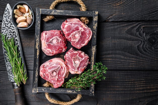 肉屋のテーブルにナイフで生の子羊の首肉。黒の木製の背景。上面図。スペースをコピーします。