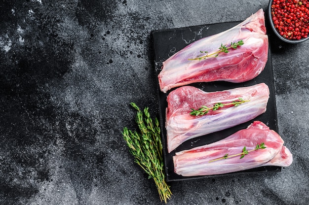 Carne cruda degli stinchi di agnello su una tavola di marmo. sfondo nero. vista dall'alto. copia spazio.