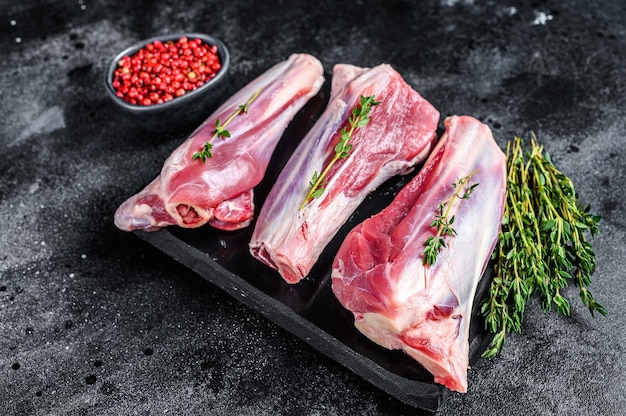 Raw lamb shanks meat on a marble board. Black background. Top view.