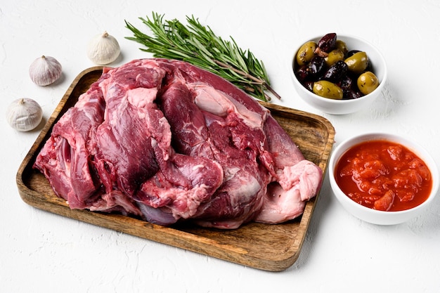 Raw lamb shoulder meat ready for baking with ingredients and herbs on white stone table background with copy space for text