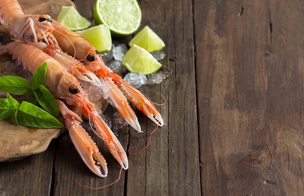 Raw langoustine on ice with lime and basil  on dark wooden table close up with copy space