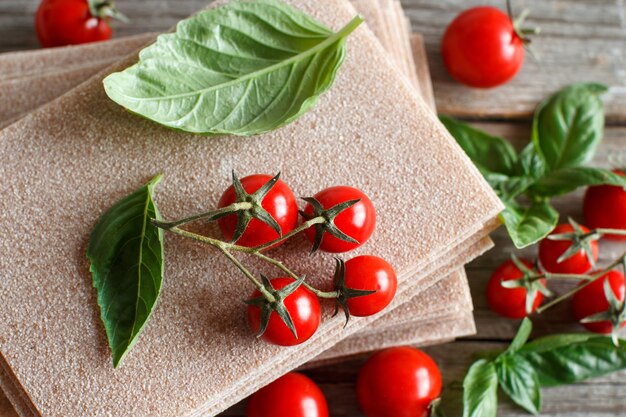 Raw lasagna sheets,basil and cherry tomatoes on a wooden table