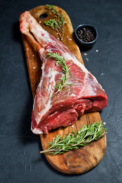 Un cosciotto d'agnello crudo su un tagliere di legno. rosmarino, timo, pepe nero.