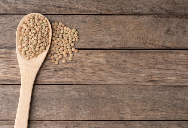 Raw lentils on a spoon over wooden table with copy space