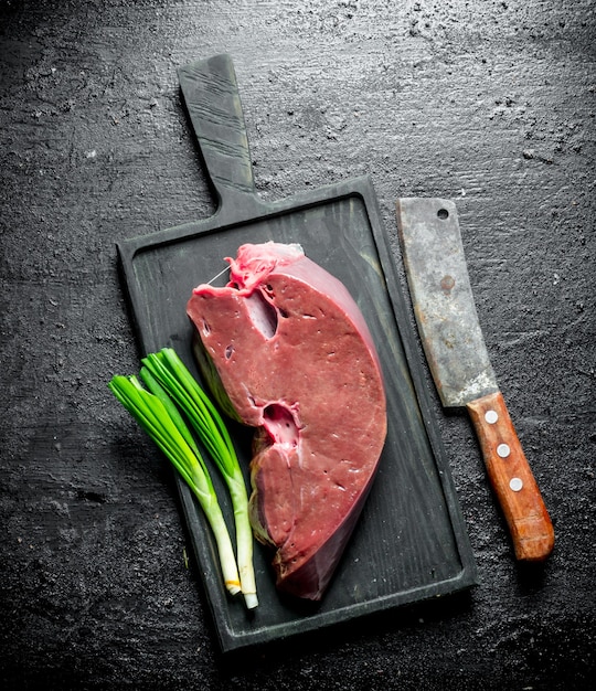 Raw liver on a cutting Board with green onions. On black rustic surface