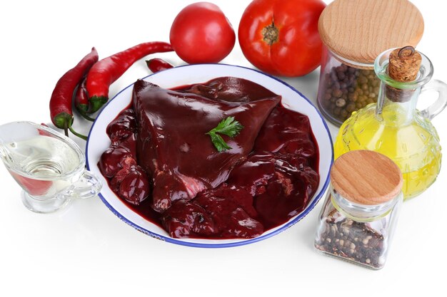 Raw liver on plate with spices and condiments isolated on white