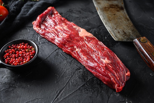 Foto machete crudo noto anche come carne di fajita di bistecca di bistrot o onglet vicino al coltello da macellaio con pepe rosa e rosmarino sfondo nero vista laterale