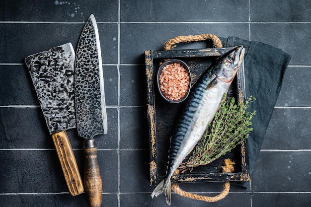 木製トレイにハーブとスパイスを入れたサバの生魚を調理する準備ができている黒の背景トップ ビュー