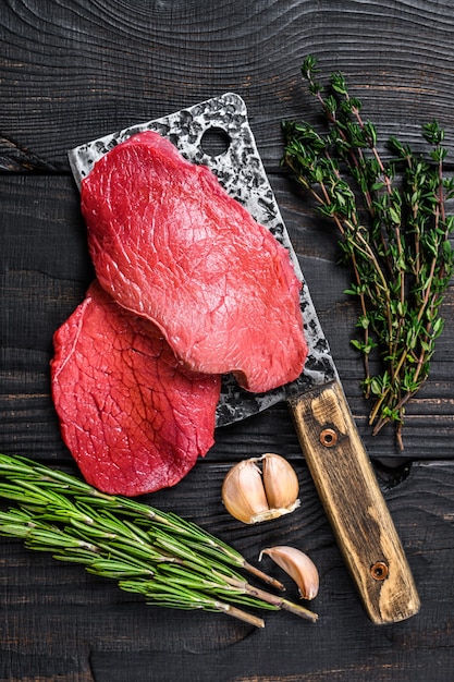 Raw marble beef meat fillet steak on butcher cleaver. black
wooden background. top view.