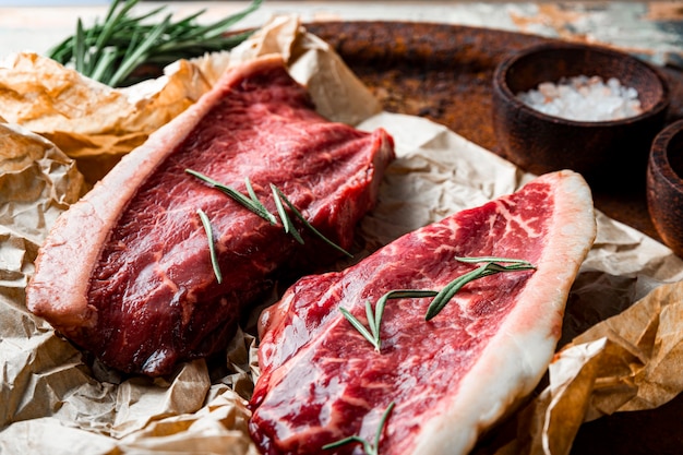 Raw marbled beef steaks and seasonings for their preparation on the old wooden background. Raw beef meat on the kitchen table. High quality photo