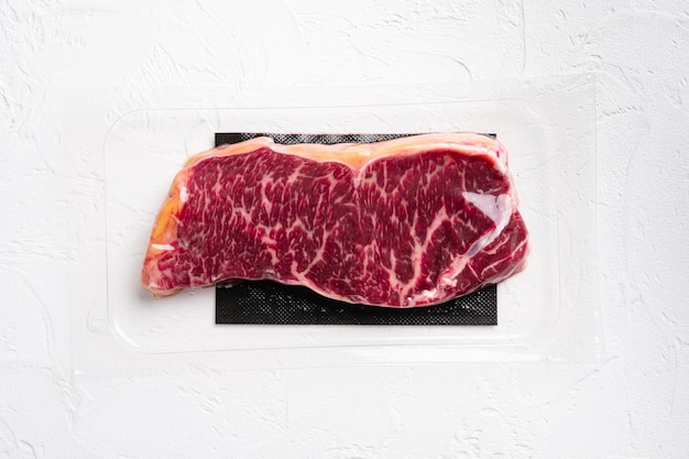 Raw marbled beef steaks in vacuum pack set, on white stone table background, top view flat lay, with copy space for text