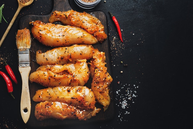 Raw marinated chicken breast on dark surface with spices ready to cook