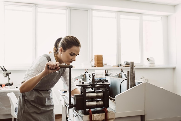 Raw material processing female woman goldsmith crafting metal on craft rolling machine