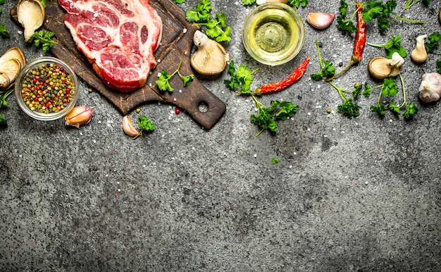 生肉の背景。素朴なテーブルの上に香りのよいスパイスと新鮮なハーブを添えた生のポークチョップ。