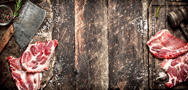 Raw meat background. Pieces of raw steak with spices and herbs on rustic table.