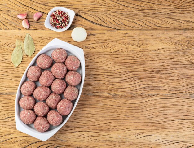 Raw meat balls on a white plate with seasonings and copy space